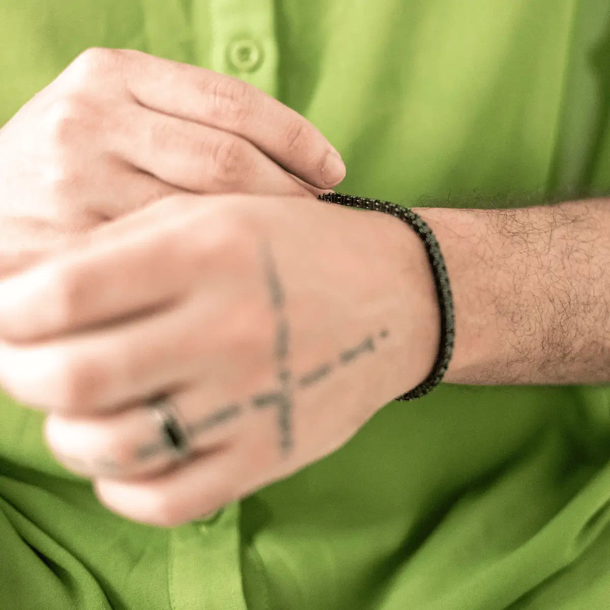 homem-com-camisa-verde-usando-pulseira-masculina-riviera-preta-no-pulso-com-tatuagem-na-mao